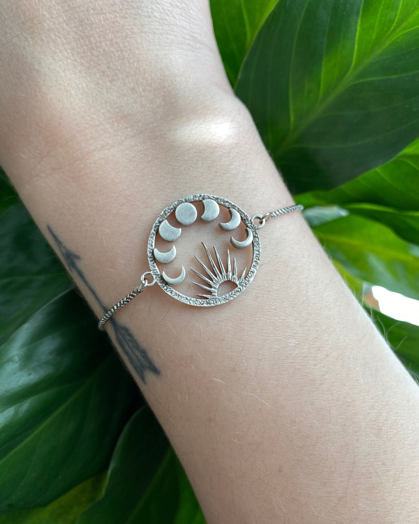 Silver bracelet with moon phases on a wrist against a green leafy background