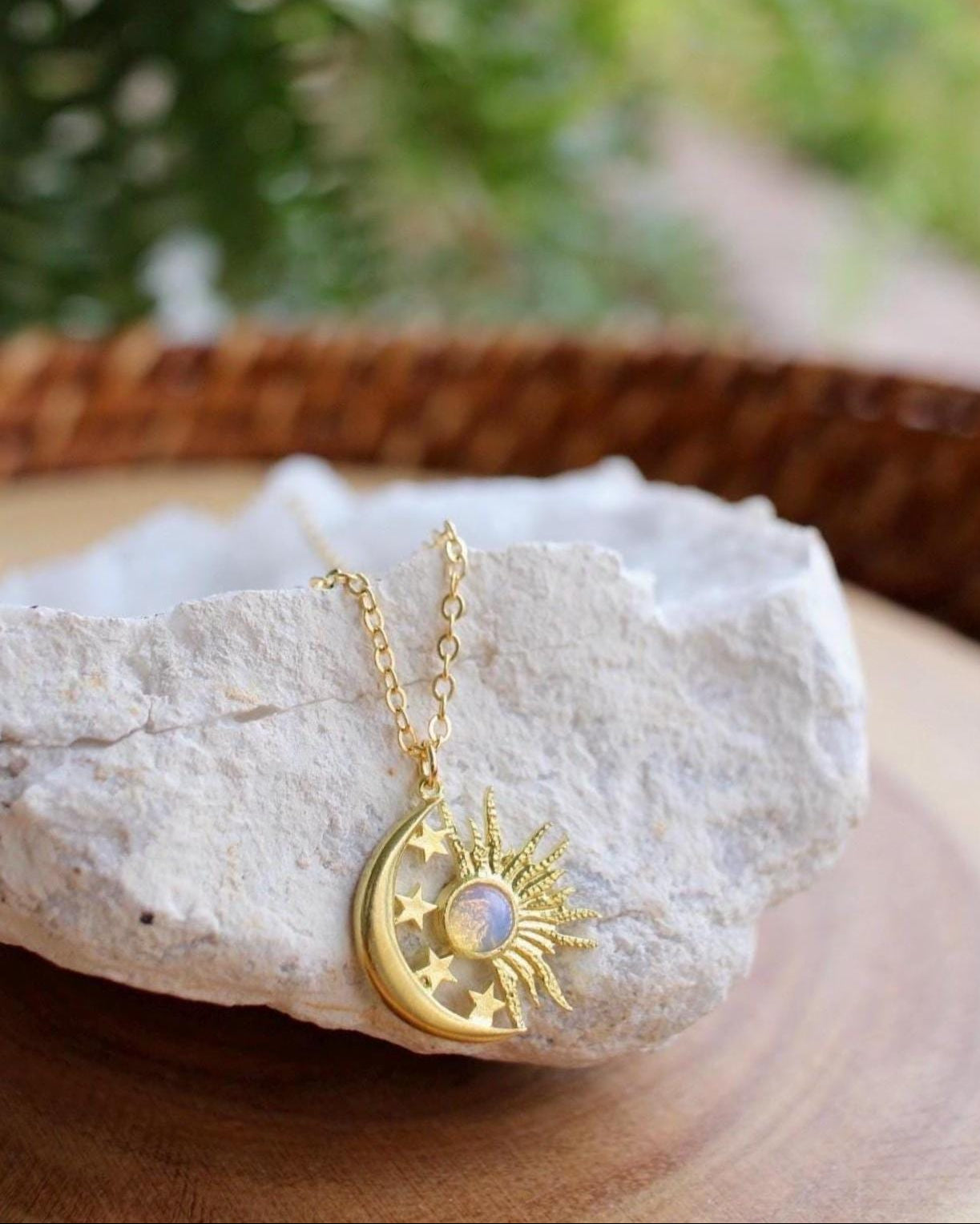 Gold necklace with a moon and sun pendant on a rock with a blurred natural background