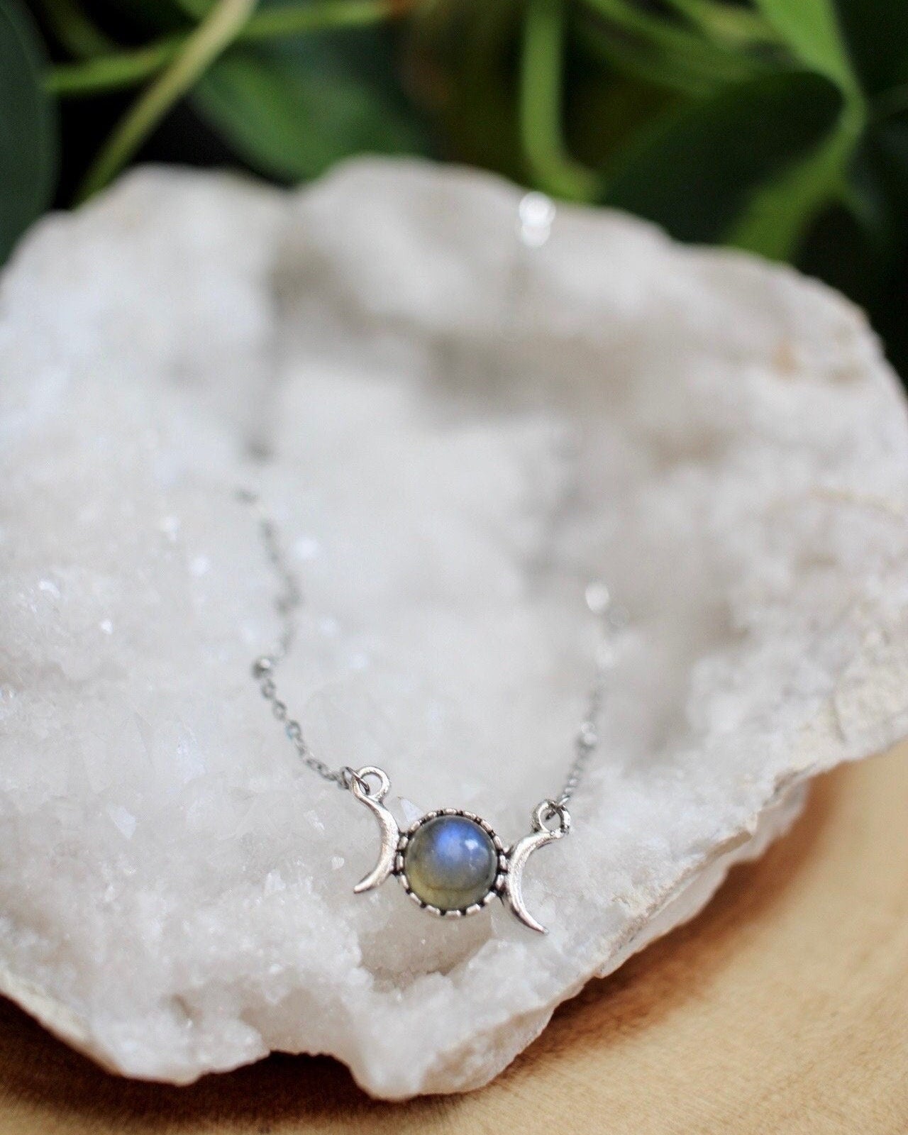 Necklace with a triple moon pendant on a white stone with greenery in the background