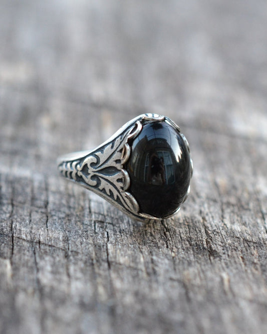 Silver ring with a black stone on a wooden surface