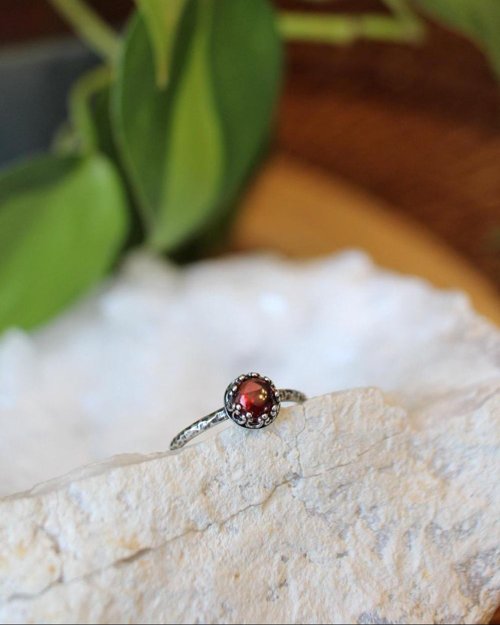 Ring with a red gemstone on a white stone surface with green leaves in the background