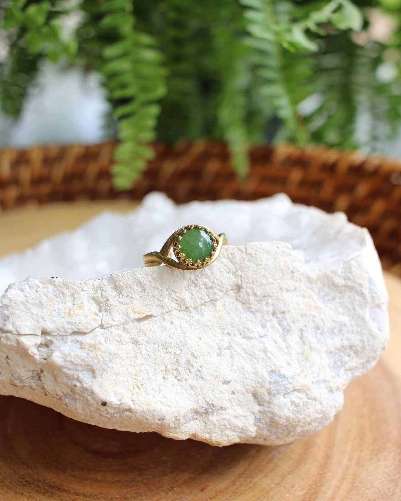 Gold ring with a green gemstone on a rock with ferns in the background