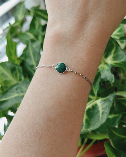 Bracelet with a green gemstone on a wrist against a green plant background