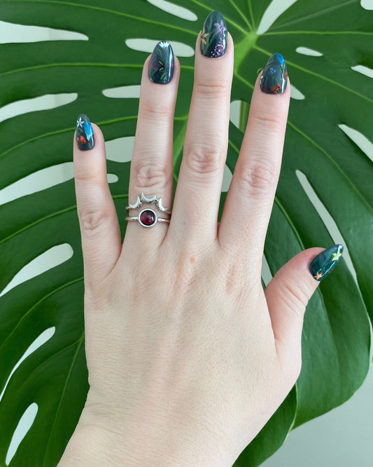 Hand wearing a ring with a red gemstone against a green leaf background