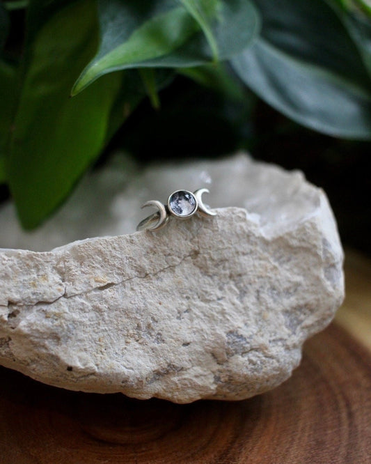 Silver ring with a full moon on a rock with green leaves in the background