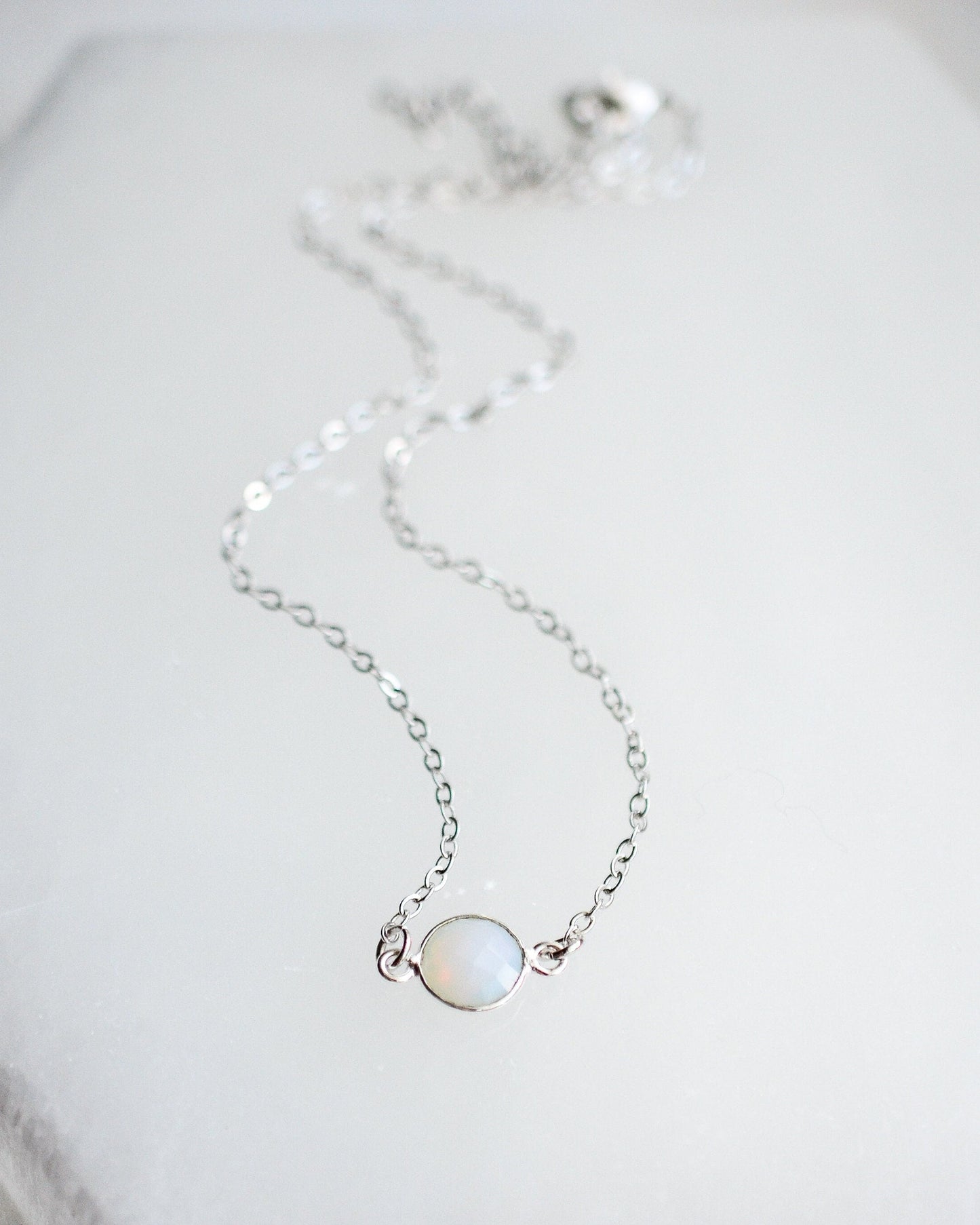 Delicate silver necklace with a small round opalite gemstone on a light background