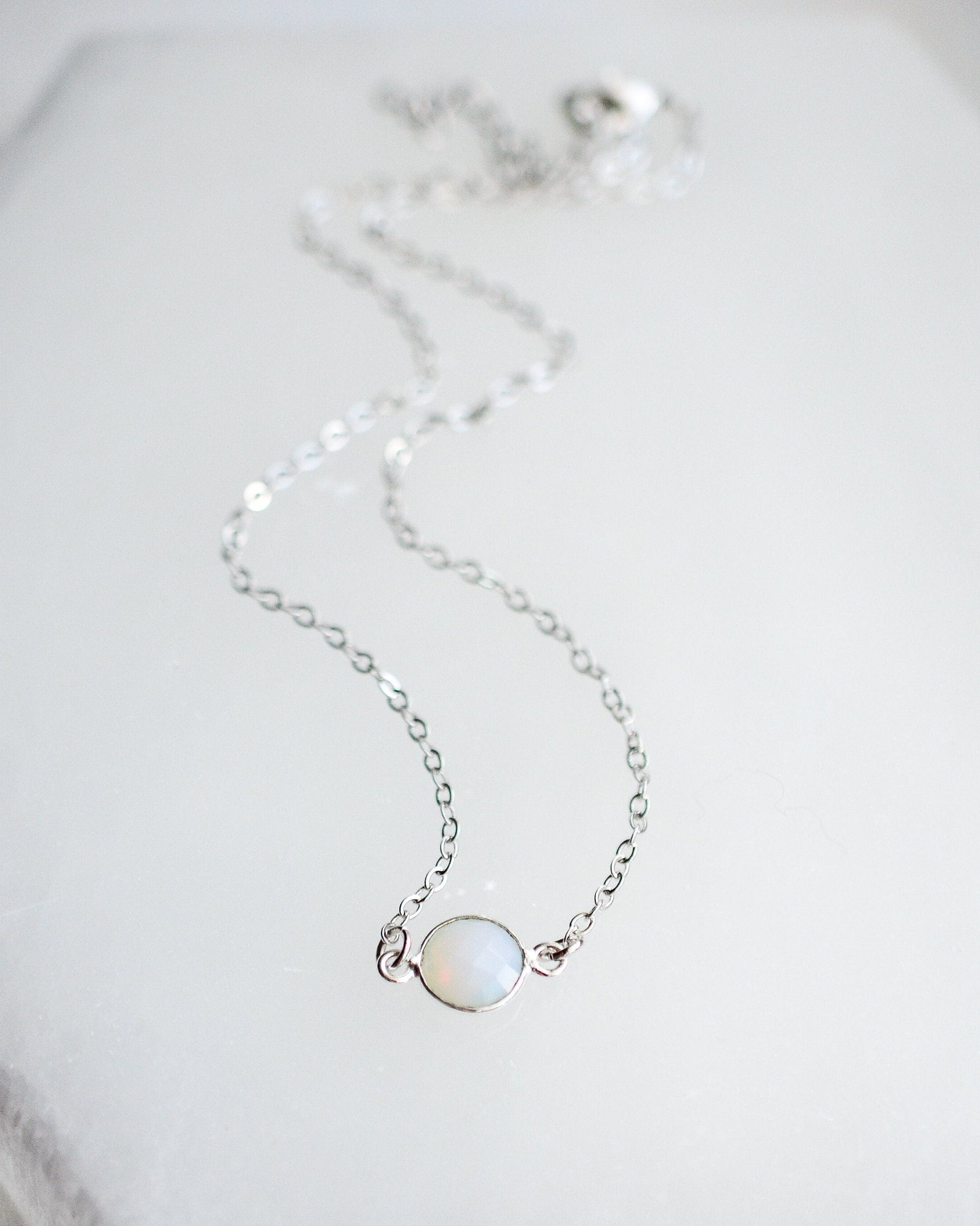 Delicate silver necklace with a small round opalite gemstone on a light background