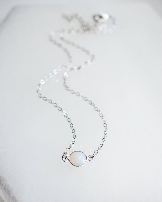 Delicate silver necklace with a small round opalite gemstone on a light background