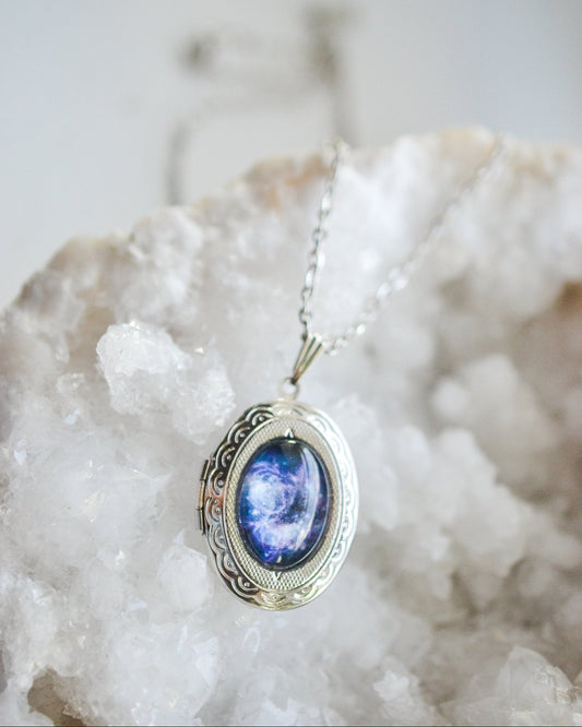 Silver necklace with a blue and purple galaxy pendant on a white stone background