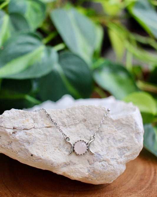 Necklace with a pink stone pendant on a rock with green leaves in the background