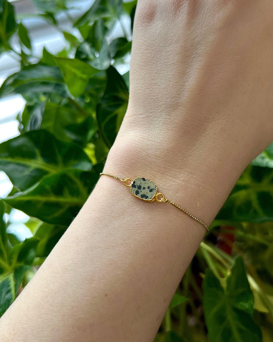 Gold bracelet with a rectangle gold plated gemstone on a wrist against a green leafy background