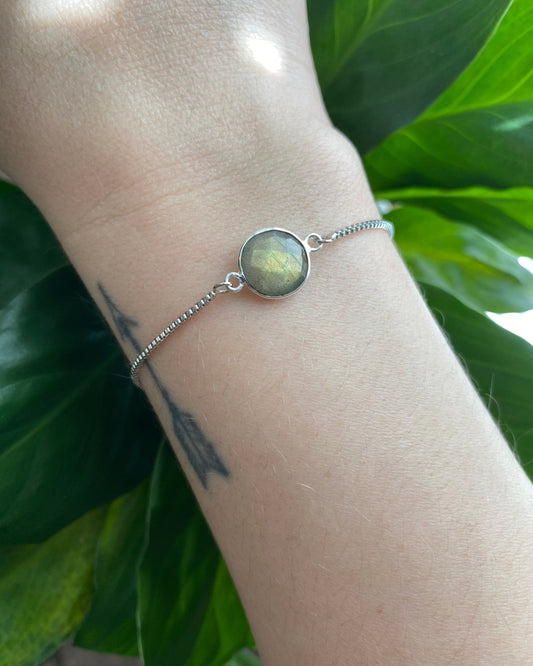 Bracelet with a round green stone on a wrist against a green leafy background