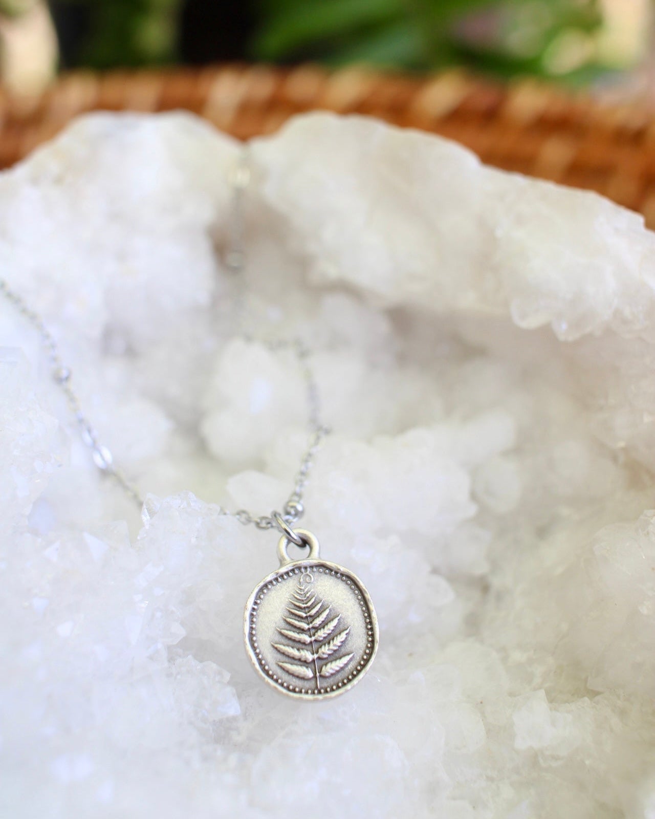 Silver necklace with a fern leaf charm on a white stone surface