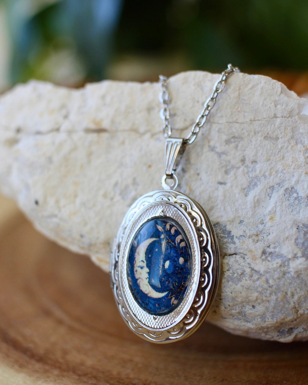 Silver necklace with a blue crescent moon locket pendant on a stone surface