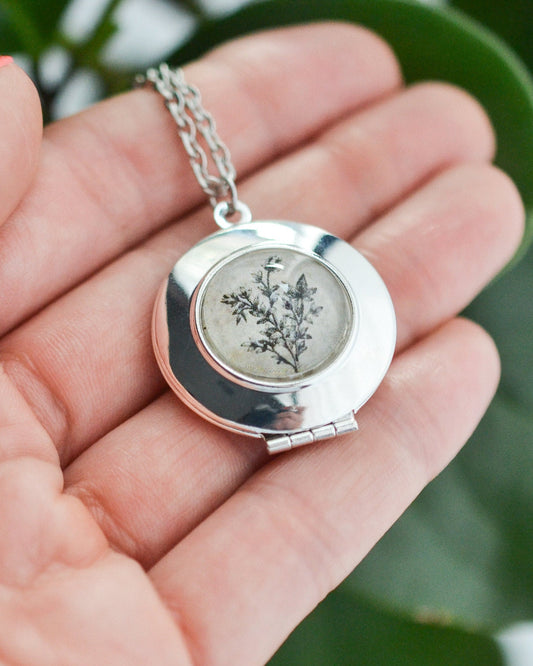 Silver pendant with a botanical design on a hand in front of a plant