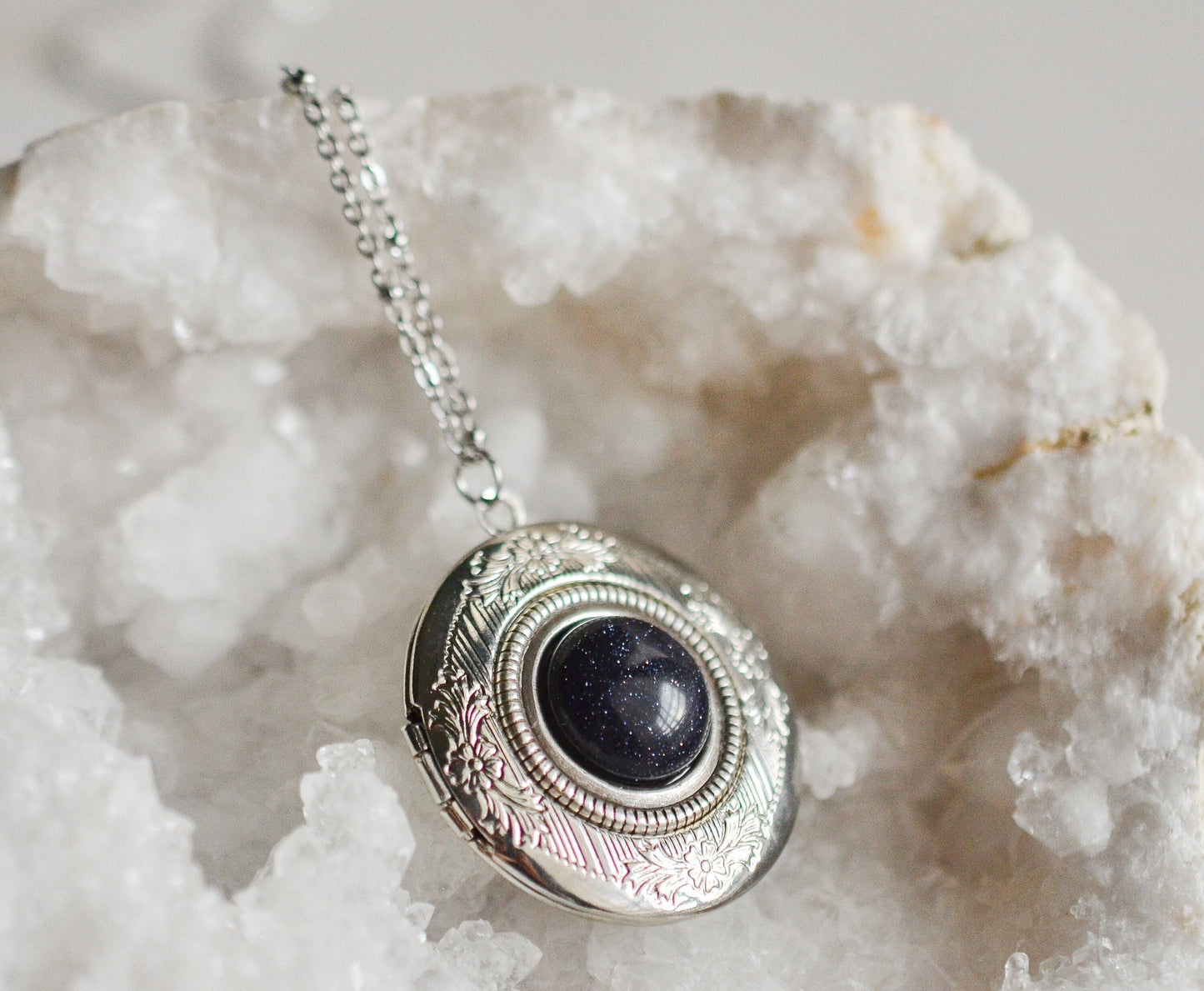 Silver necklace with a blue shimmery stone pendant on a white crystal background