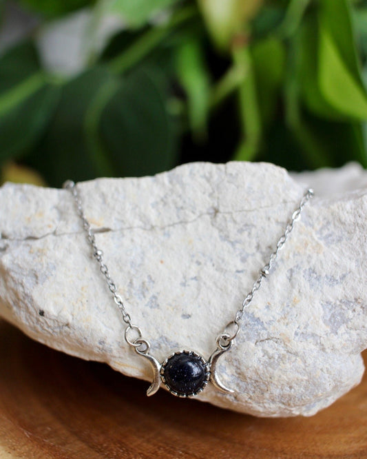 Necklace with a dark blue gemstone on a rock with greenery in the background