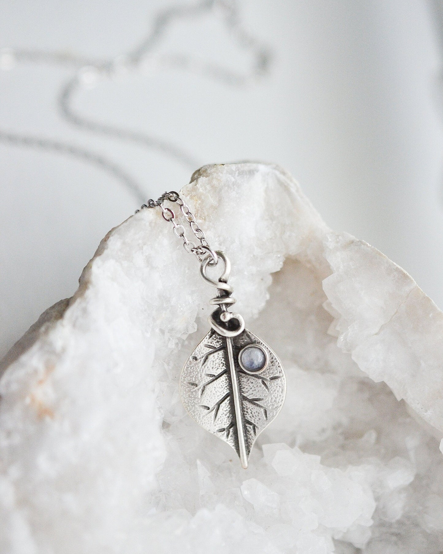 Silver leaf-shaped pendant necklace on a white crystal background