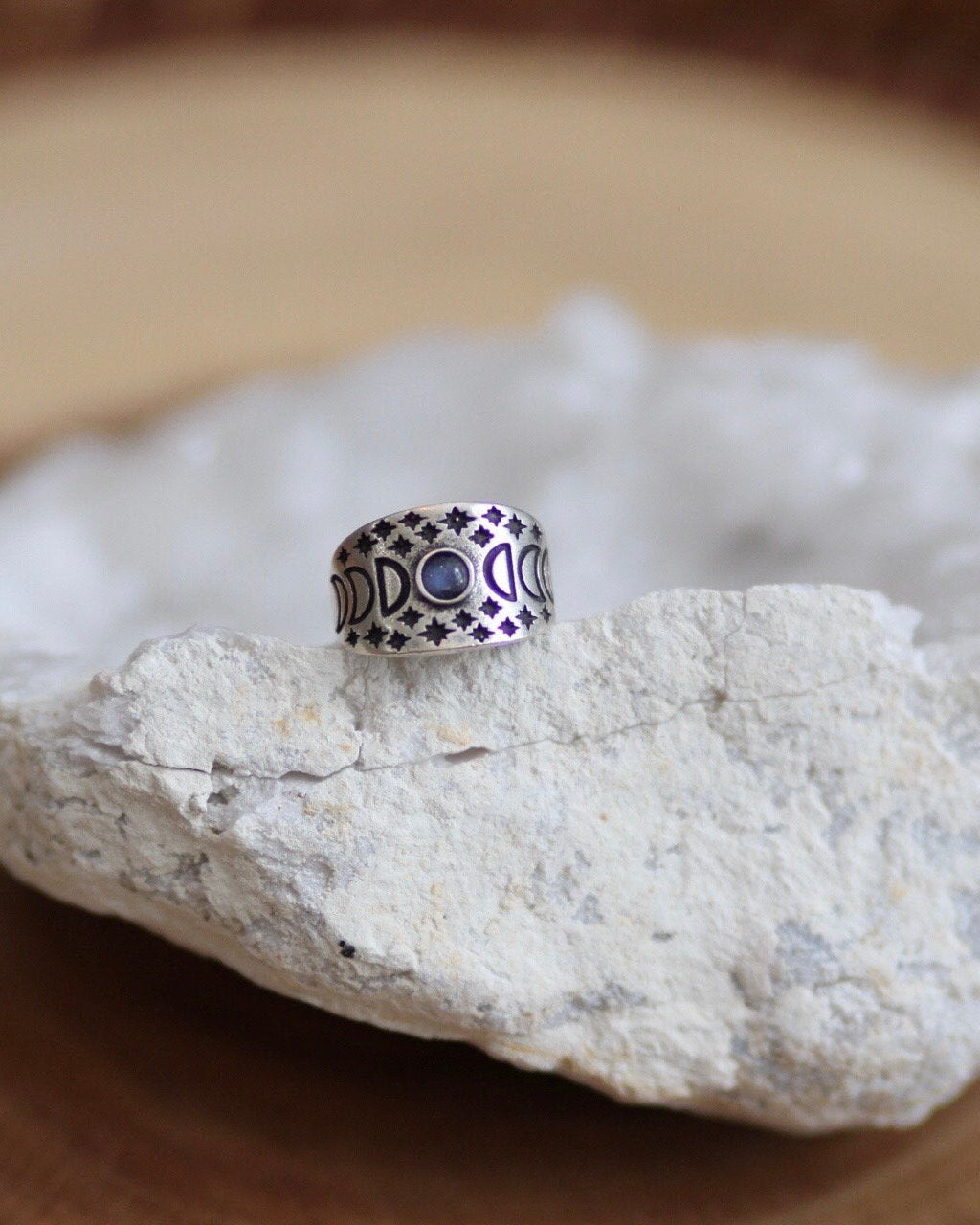 Silver ring with moon phases and star engravings and moonstone in the center on a white geode stone with wood background
