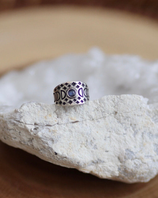 Silver ring with moon phases and star engravings and moonstone in the center on a white geode stone with wood background