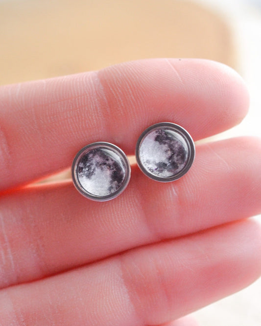 Full moon earrings held between fingers against a blurred background