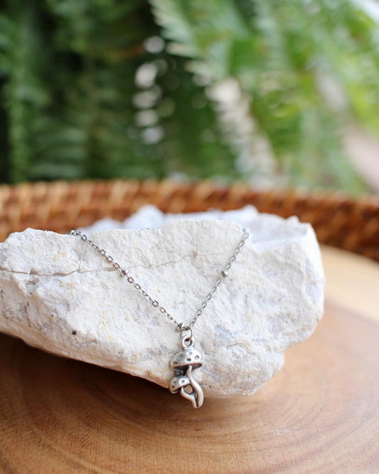 Silver mushroom charm necklace on a rock with a natural background