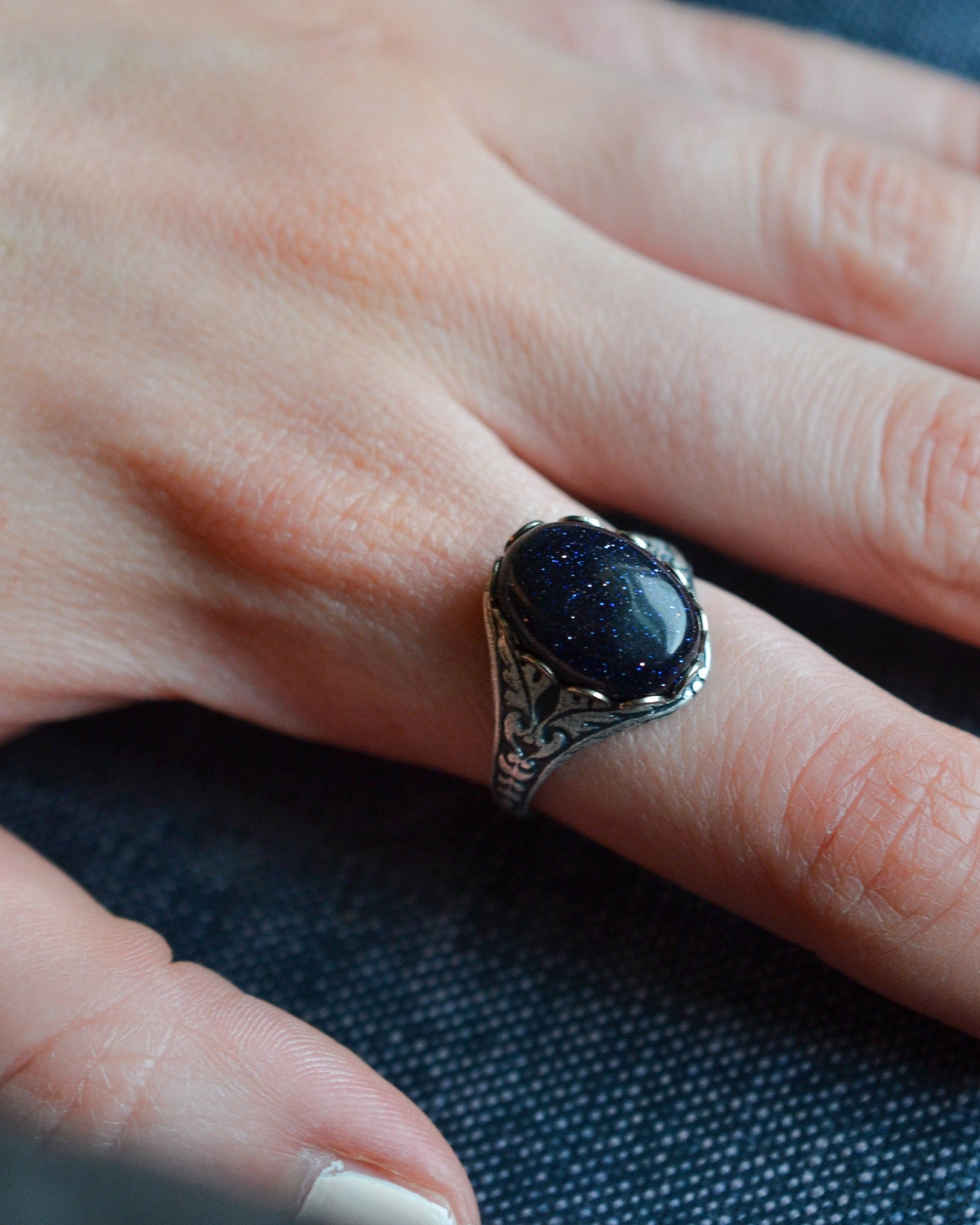 Hand wearing a ring with a dark stone on a textured background