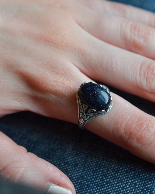 Hand wearing a ring with a dark stone on a textured background
