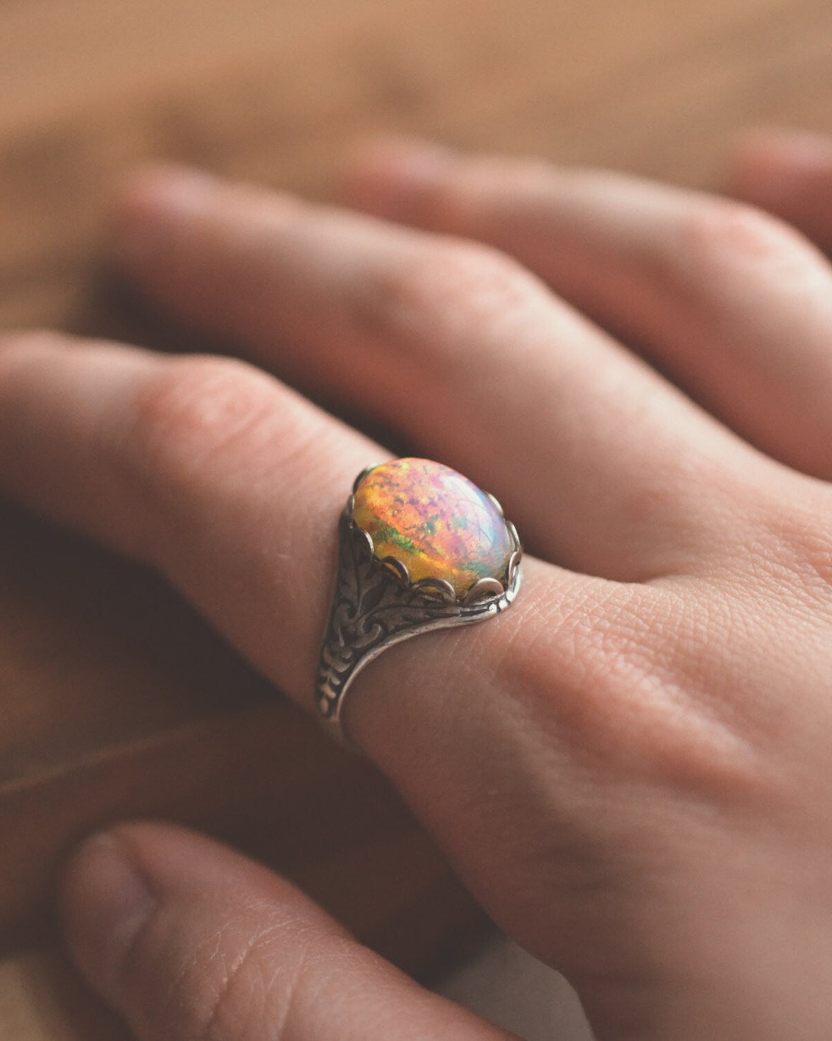 Close-up of a hand wearing an opal ring with a blurred background