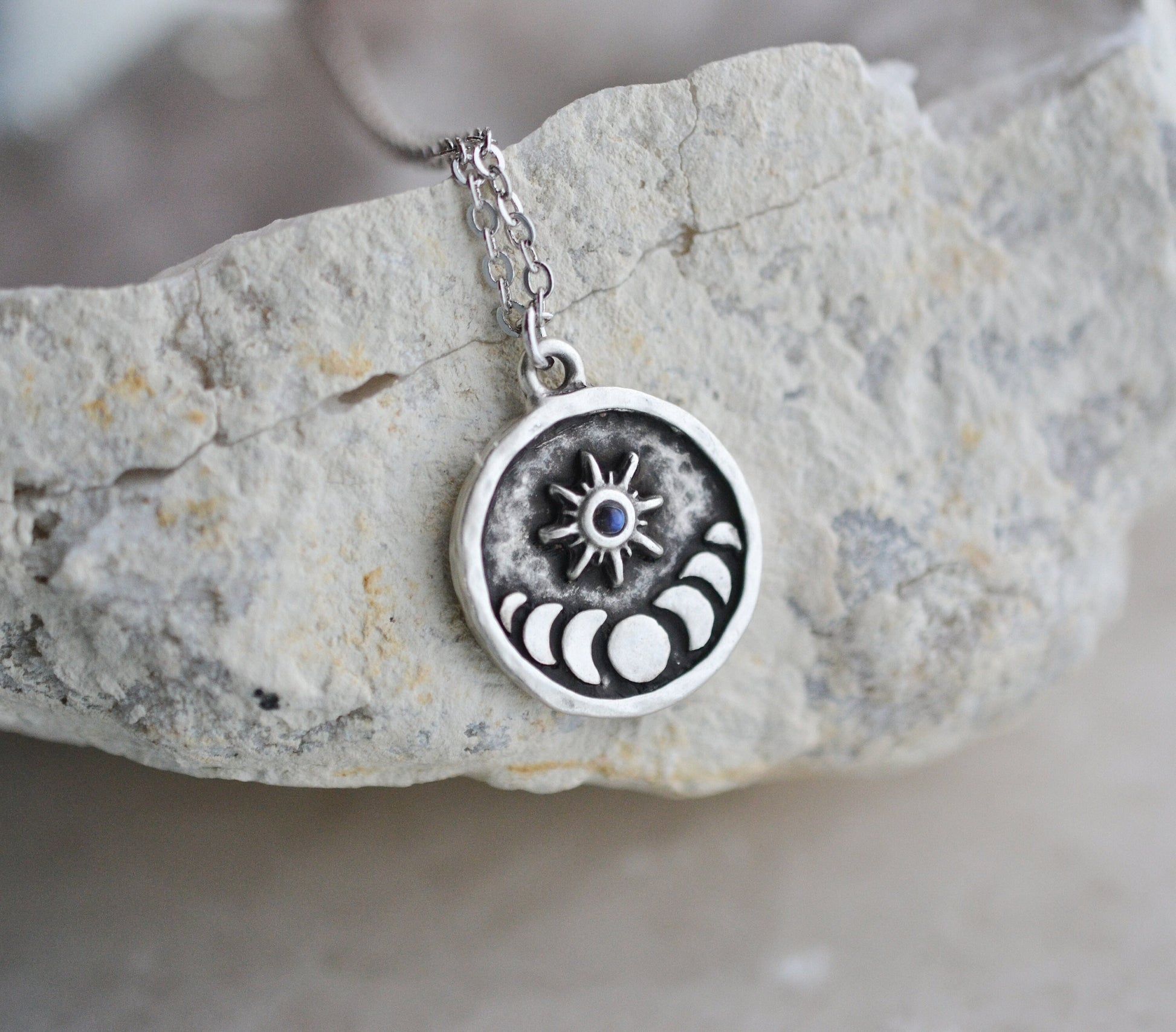 Pendant with a moon phase design and sun with a moonstone in the center attached to a chain and laying on a white geode