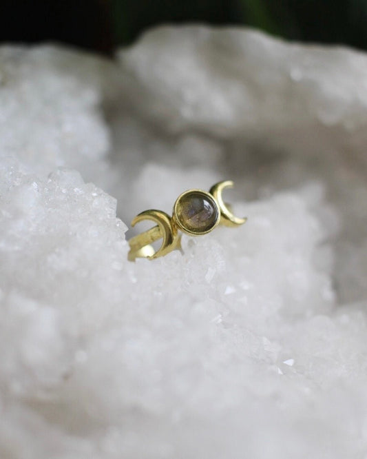 Gold triple moon ring with a green blue stone in the center on a white crystal