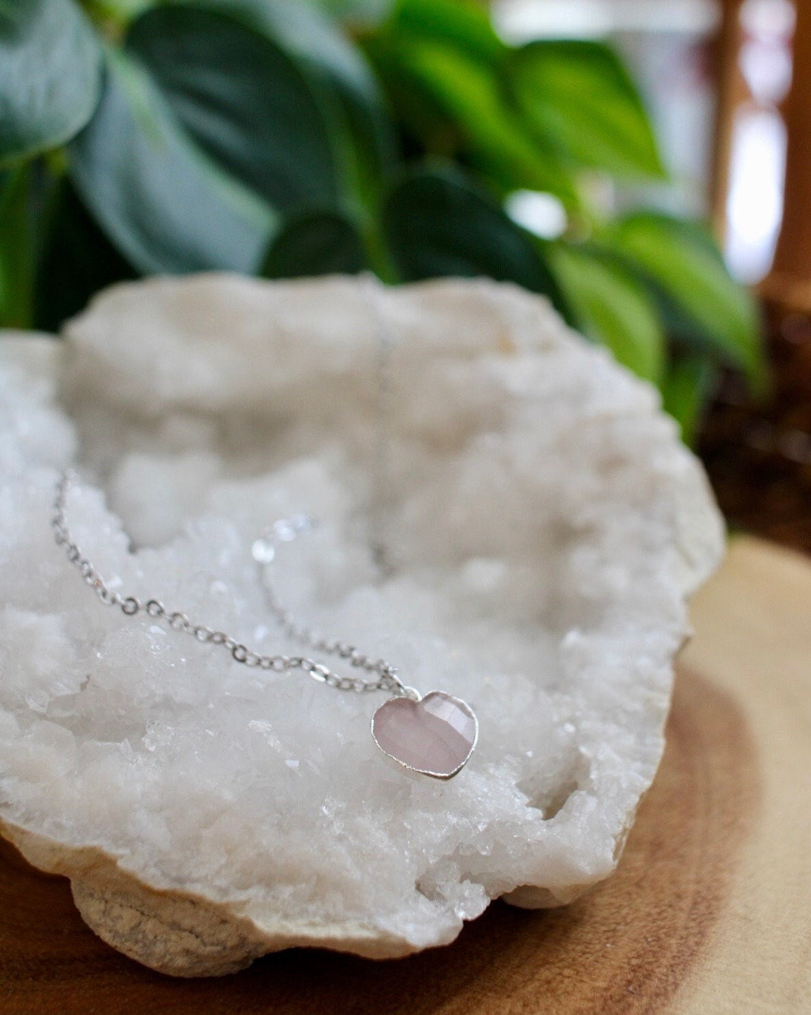 rose quartz heart necklace on a white crystal with a plant in the background