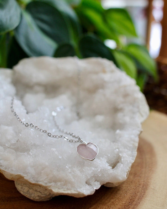 rose quartz heart necklace on a white crystal with a plant in the background