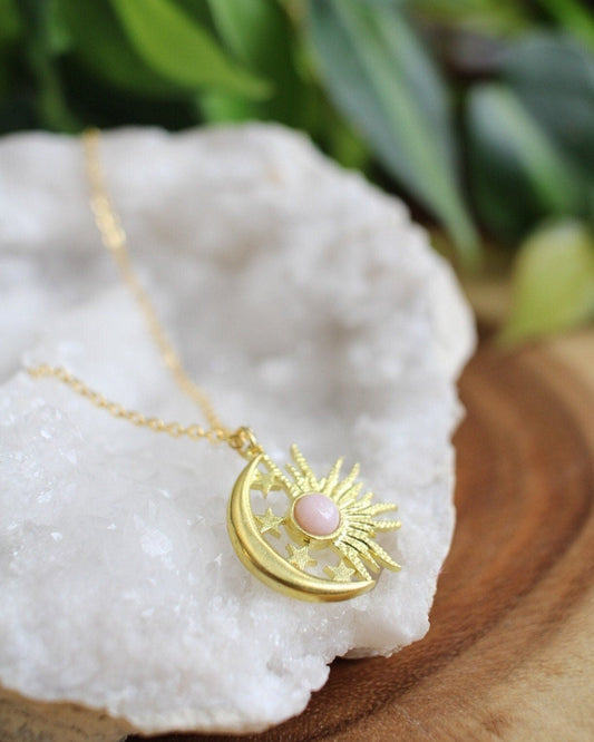 Gold necklace with a sun and moon pendant with pink stone on a white stone surface