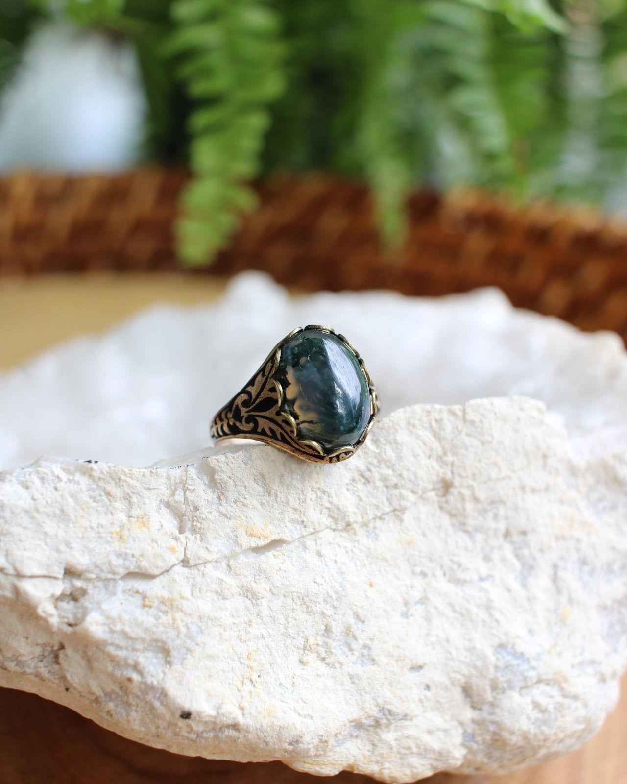 Ring with a green stone on a white rock with blurred greenery in the background