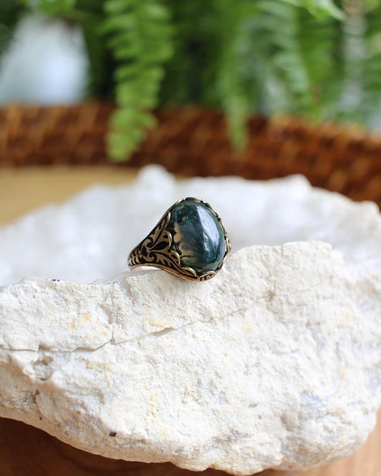 Ring with a green stone on a white rock with blurred greenery in the background