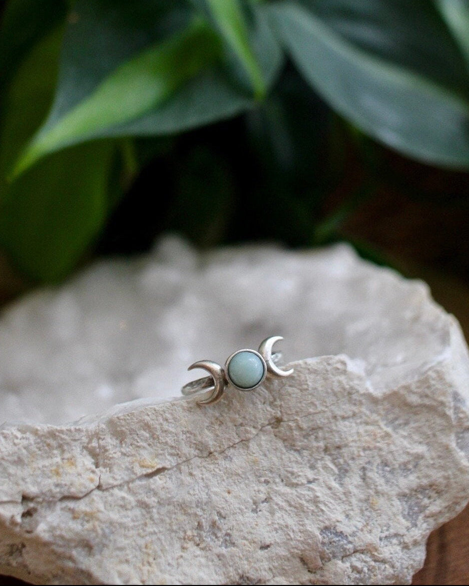 Triple moon ring with a turquoise color stone in the center sitting on a white geode with green leaves in the background
