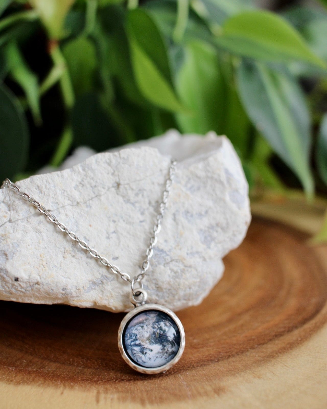Necklace with a pendant featuring an earth design, placed on a rock with green foliage in the background.