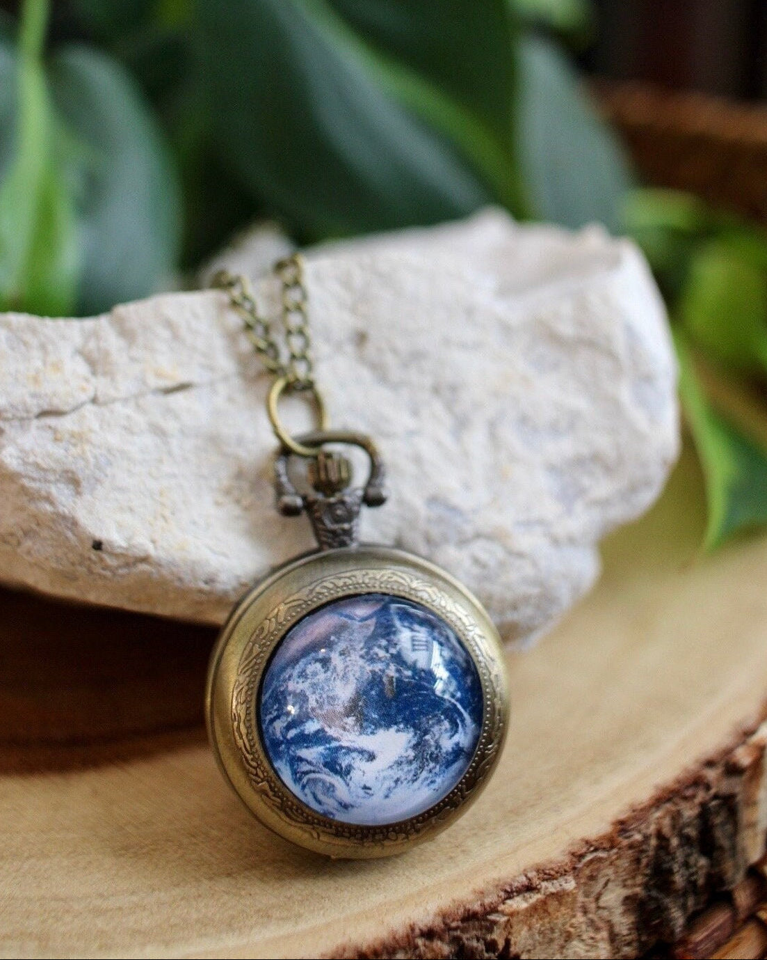 Necklace with a pendant featuring an Earth design on a wooden surface with greenery in the background