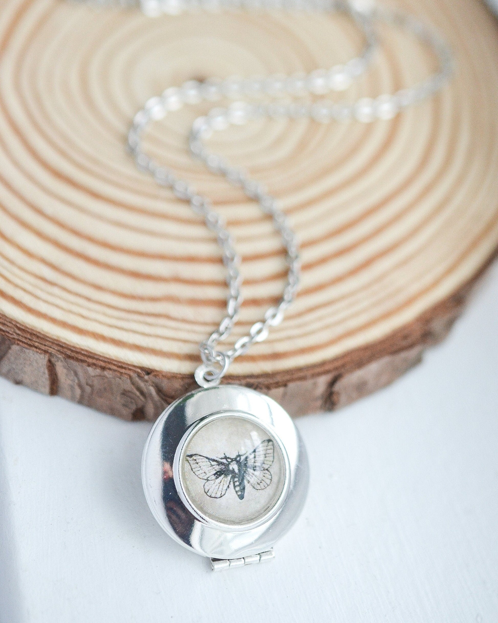 Silver locket necklace with a butterfly design on a wooden surface