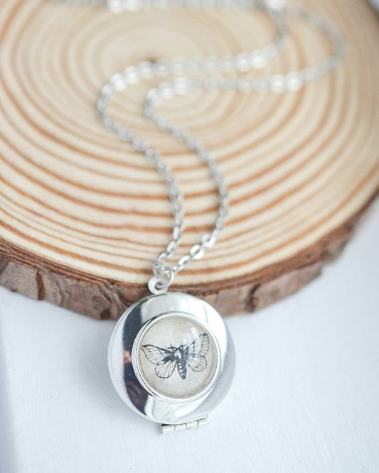 Silver locket necklace with a butterfly design on a wooden surface