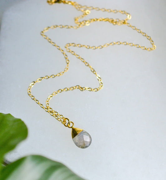 Gold necklace with a teardrop-shaped labradorite crystal pendant on a light background