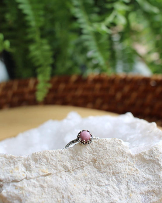 Ring with a pink gemstone on a white stone surface with green foliage in the background