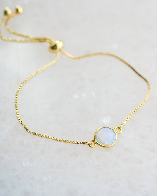 Gold bracelet with a round opal stone on a light crystal background