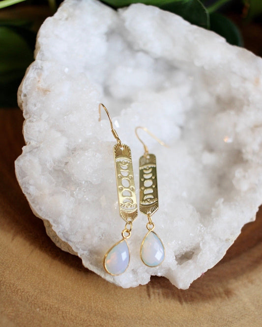 Gold earrings with teardrop-shaped gemstones on a white stone surface