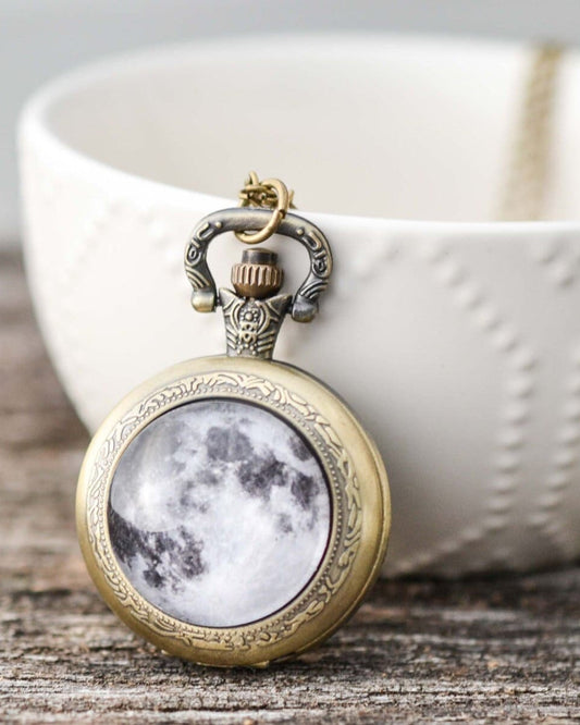 Decorative pocket watch necklace with moon design on a wooden surface