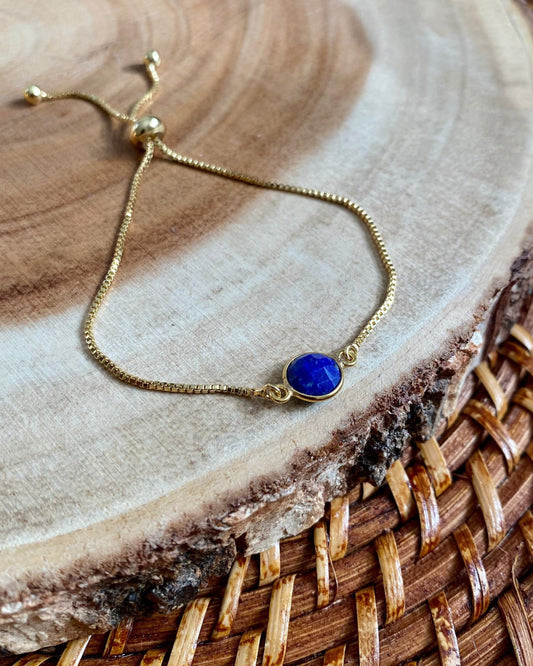 Gold bracelet with a blue stone on a wooden surface
