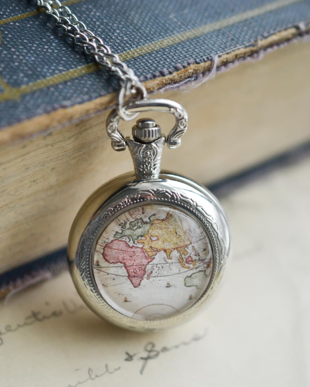 Silver pocket watch with world map design on a textured surface