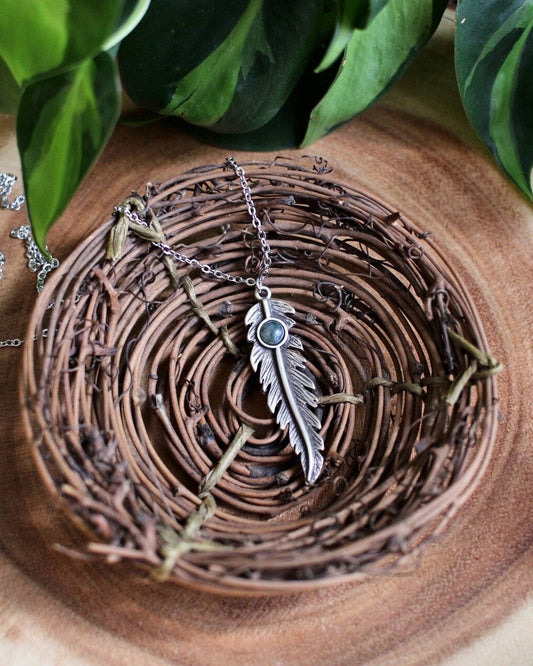 Silver feather necklace on a wooden surface with green leaves in the background