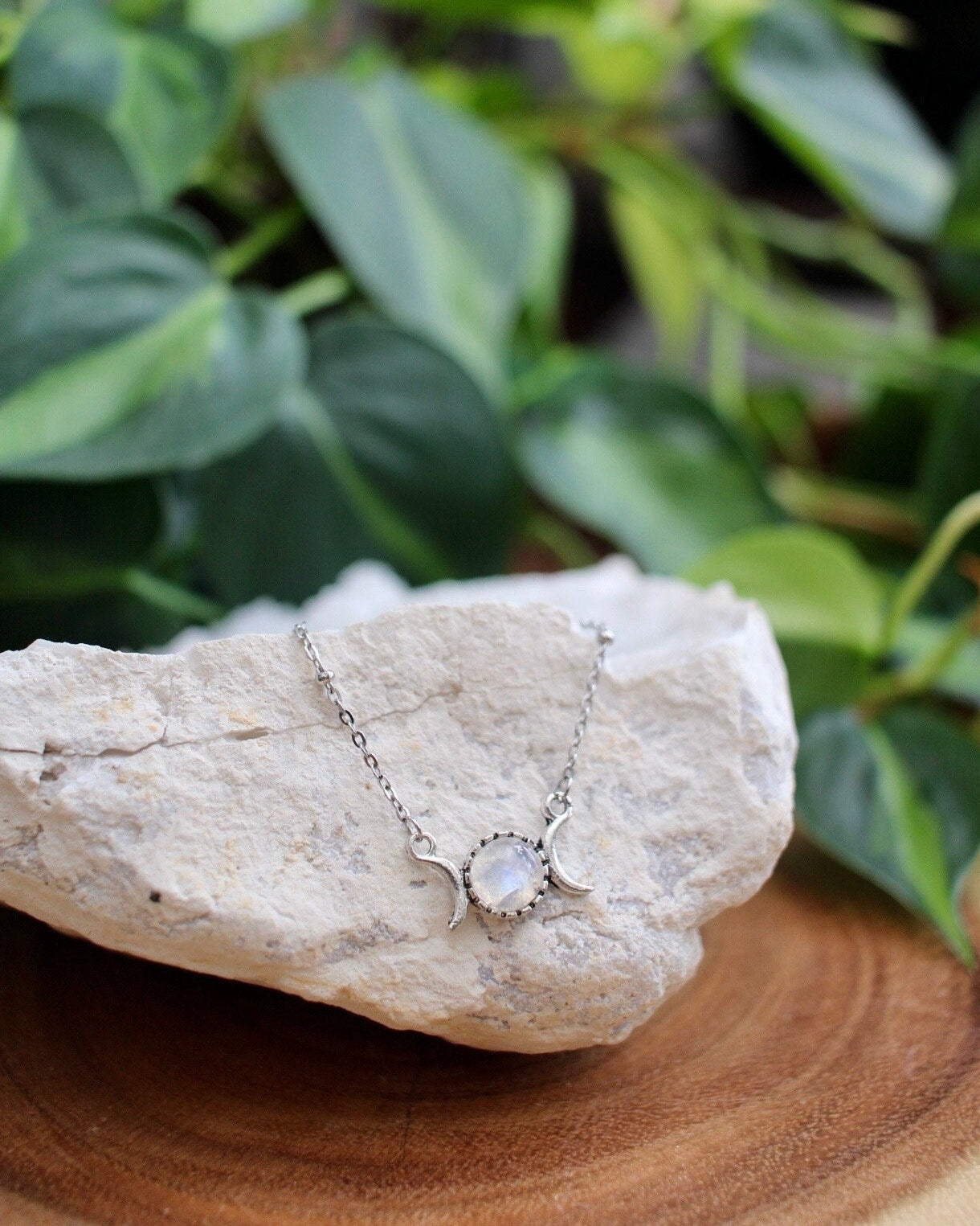 Silver necklace with a triple moon charm on a rock in front of green foliage